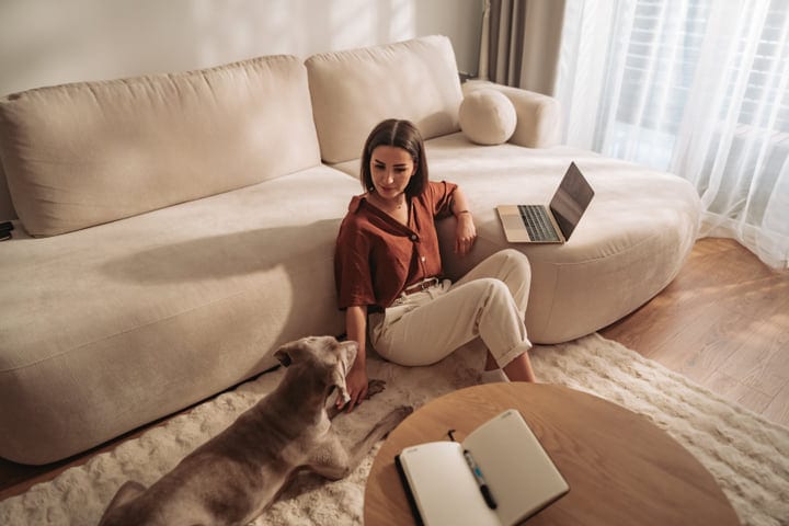 Woman Working On Laptop Next To Her Dog In Living Room