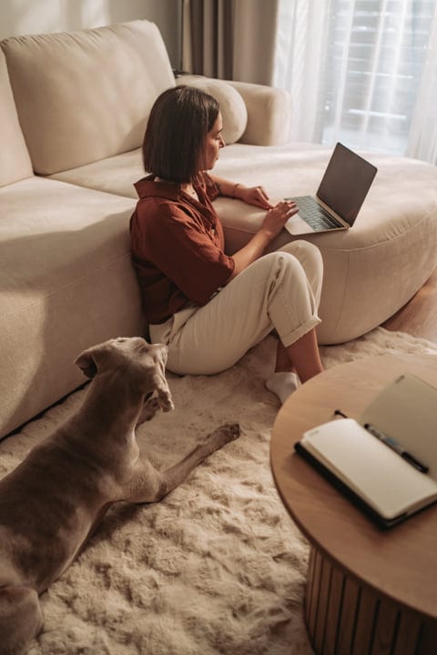 Focused Woman Using Laptop On Living Room Floor Beside Her Pet Dog