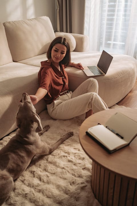 Woman Stroking Her Dog While Sitting On The Floor With A Laptop