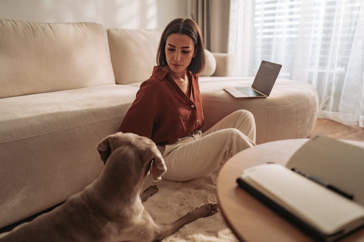 Woman Relaxing On Floor With Dog And Laptop In Modern Living Room