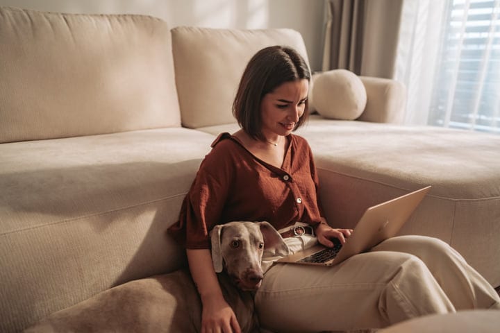 Woman Works From Home On Laptop With Dog On Living Room Floor