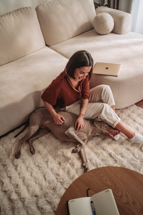 Young Woman Pets Her Dog While Relaxing On A Cozy Rug Indoors