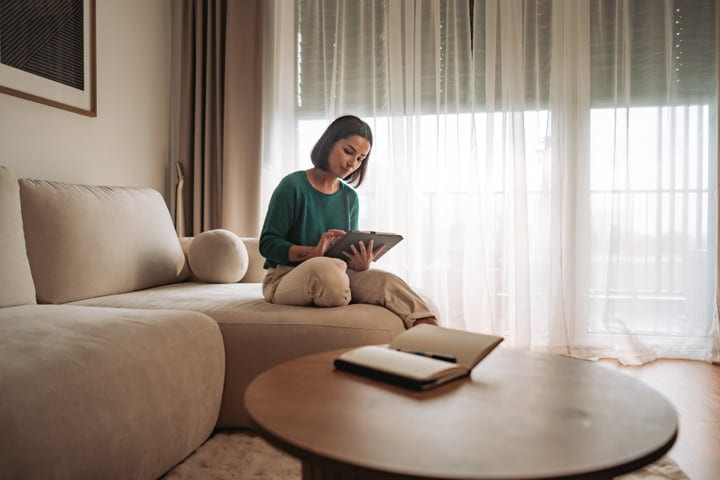Woman Sits On Sofa Using Tablet In Bright Living Room Morning