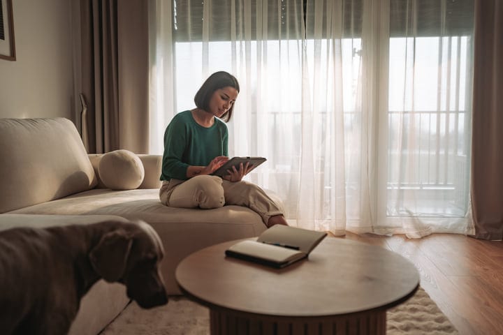 Woman Using A Tablet On Sofa By Window In Bright Living Room