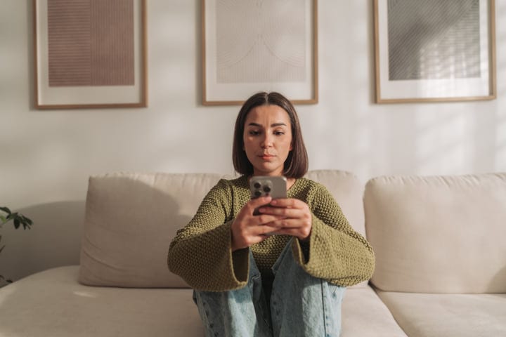 Young Woman Sits On Floor Using Smartphone In Modern Living Room