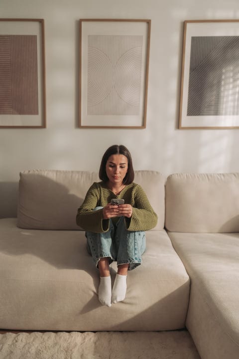 Woman In Green Sweater Sitting On Floor, Browsing On Her Smartphone