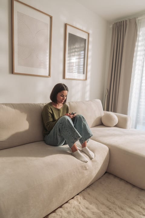 Woman Sits On Sofa Using Phone In Bright Modern Living Room