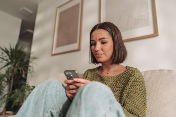 Young Woman Using Smartphone On Sofa In Her Modern Home