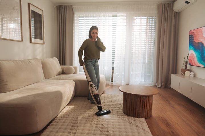 Young Woman Actively Vacuuming Plush Rug In Bright Modern Living Room