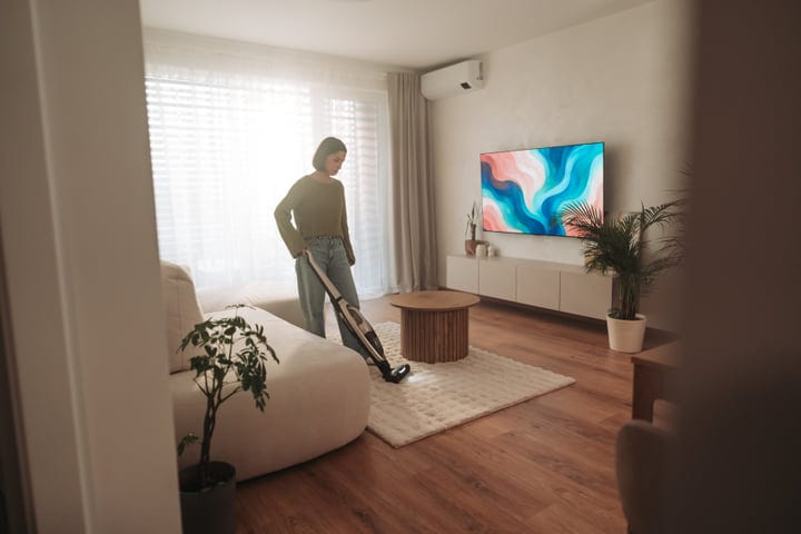 Woman Vacuuming Living Room Floor In Modern European Apartment