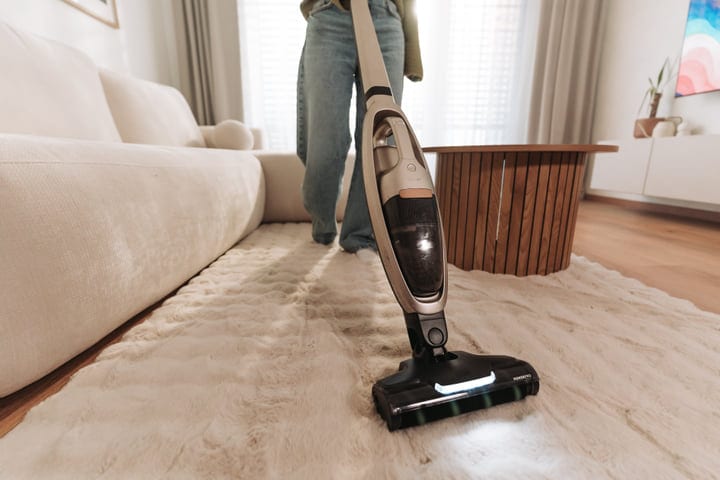 Woman Cleaning Her Fluffy Living Room Rug With A Cordless Vacuum