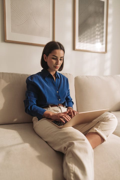 Woman Typing On Laptop While Relaxing On Sofa In Modern Home Living Room