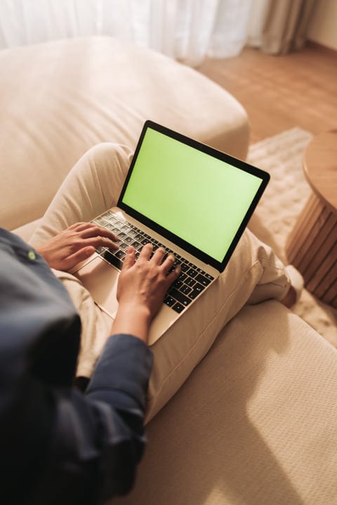 Person Typing On Laptop While Sitting Comfortably On Sofa At Home