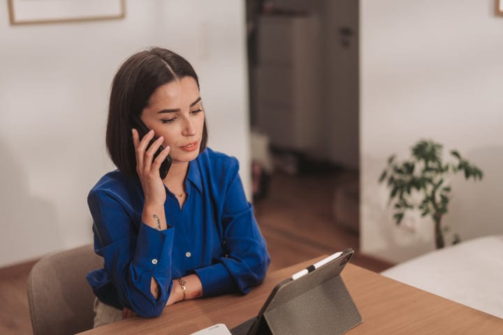 Woman Talking On Mobile Phone While Working On A Digital Tablet Indoors