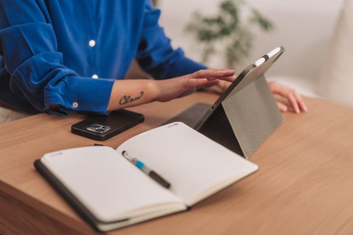 Woman Working On Tablet At Wooden Desk With Notebook And Smartphone