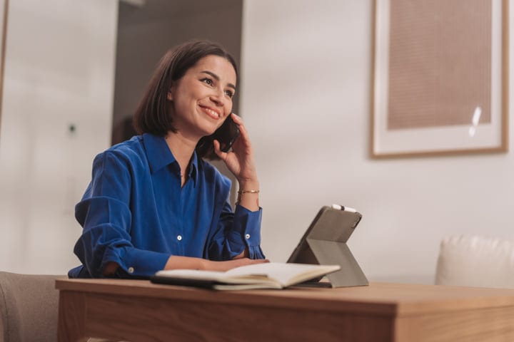 Smiling Woman Talking On Smartphone In Home Office With Tablet
