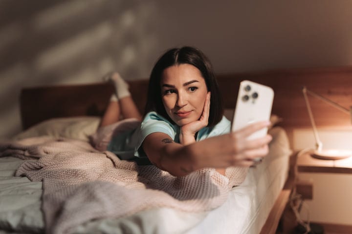Young European Woman Lying In Bed Taking A Selfie With Her Phone