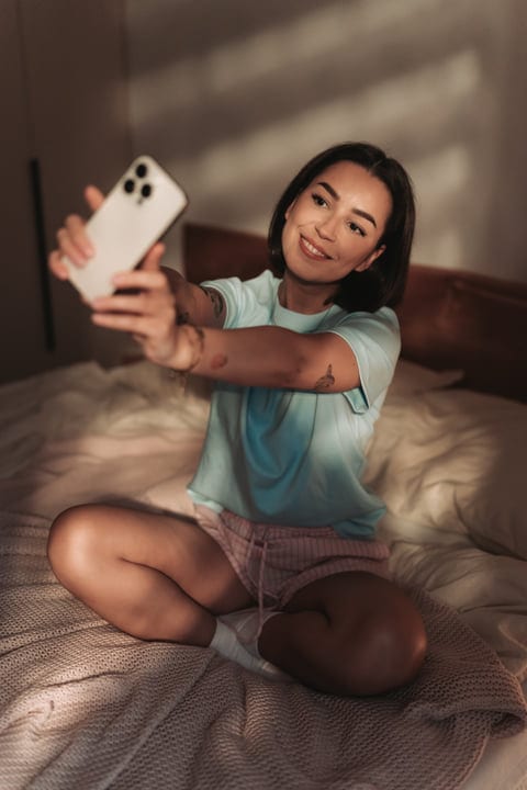 Young Woman Taking a Selfie While Sitting on Bed in Her Bedroom