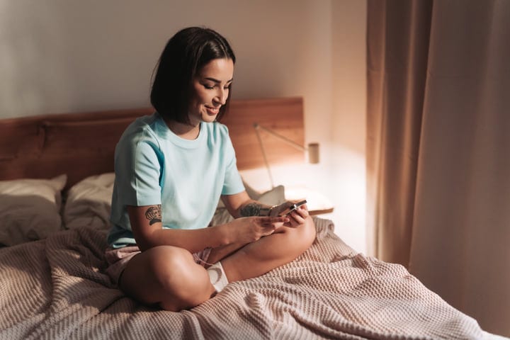 Young Woman On Bed Using Smartphone In Bright Morning Light