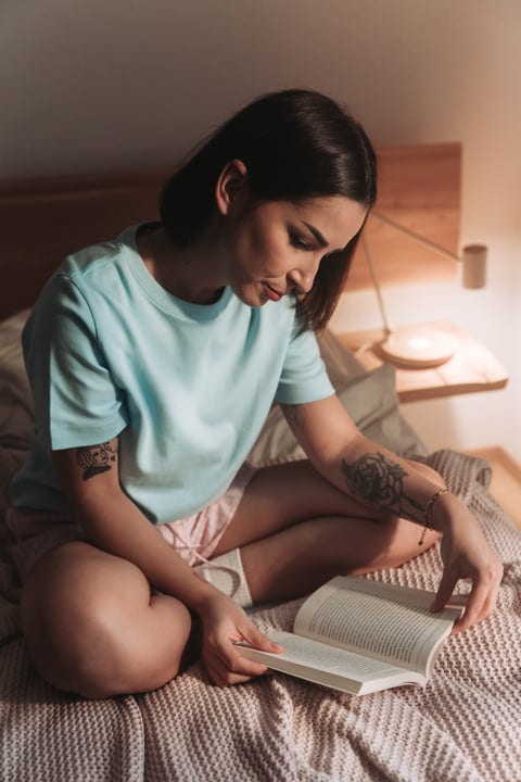 Young Woman Reading A Book Comfortably In Her Cozy Bedroom At Night