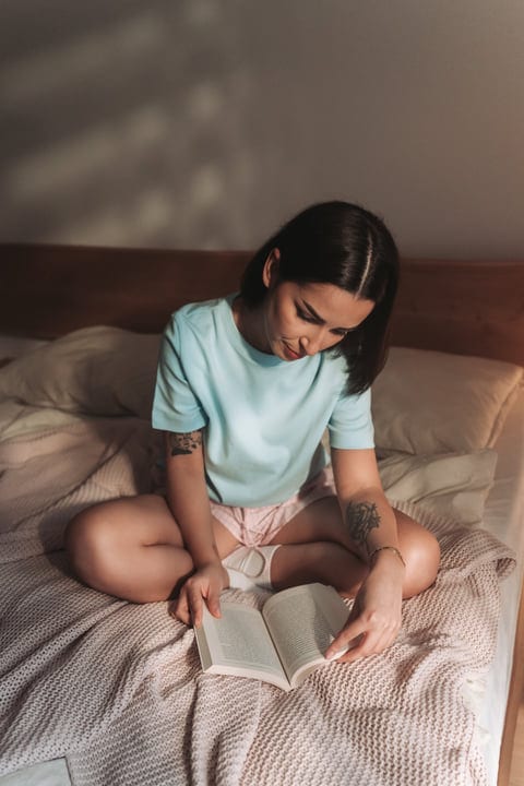Young Woman Quietly Reading A Book On Her Bed In A Cozy Room