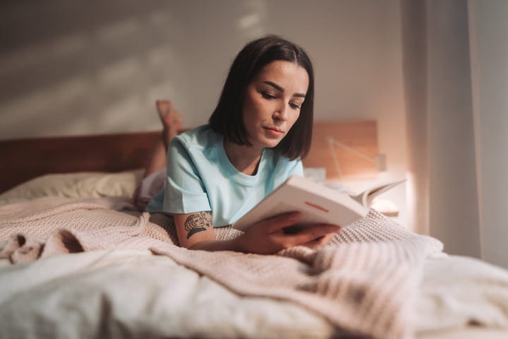 Young Woman Lies On Bed Reading A Book In Her Cozy Morning Routine