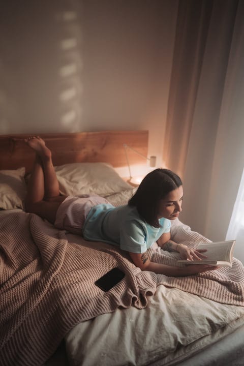Woman Reads A Book Relaxing On Her Bed In The Morning Light