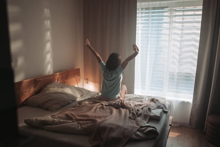 Woman Stretching In Bed Towards The Morning Sunlit Window