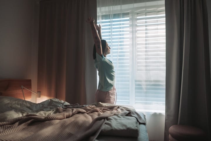 Young Woman Stretching Her Arms As She Wakes Up In A Bright Bedroom