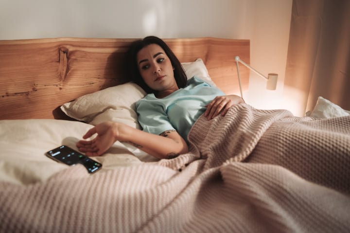 Woman Waking Up In Bed Reaching For Her Smartphone In Warm Morning Light