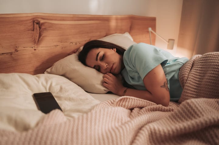 Young Woman Sleeps Peacefully In Her Cozy Bedroom With A Phone