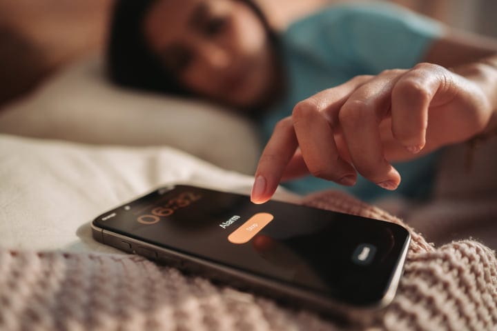 Young Woman Waking Up And Stopping Her Phone Alarm In Bed