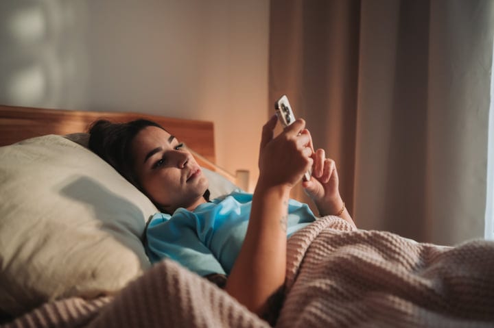 Young European Woman Browsing Smartphone Lying In Bed At Home