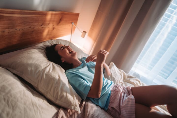 Smiling Young Woman Laughing Joyfully While Relaxing In Bed At Home