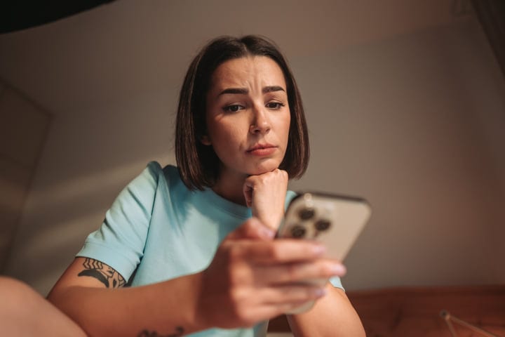 Young Woman With Thoughtful Expression Checking Her Smartphone In A Warm Lit Room