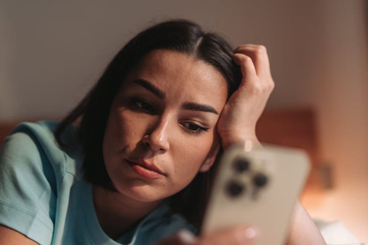 Young Woman Rests Head On Hand Browsing Smartphone In Morning Light Indoors