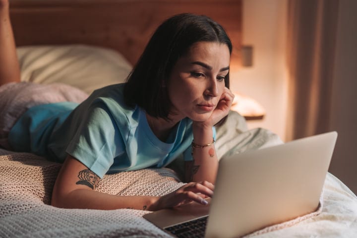 Young Woman Lying on Bed Using Laptop in Soft Morning Light