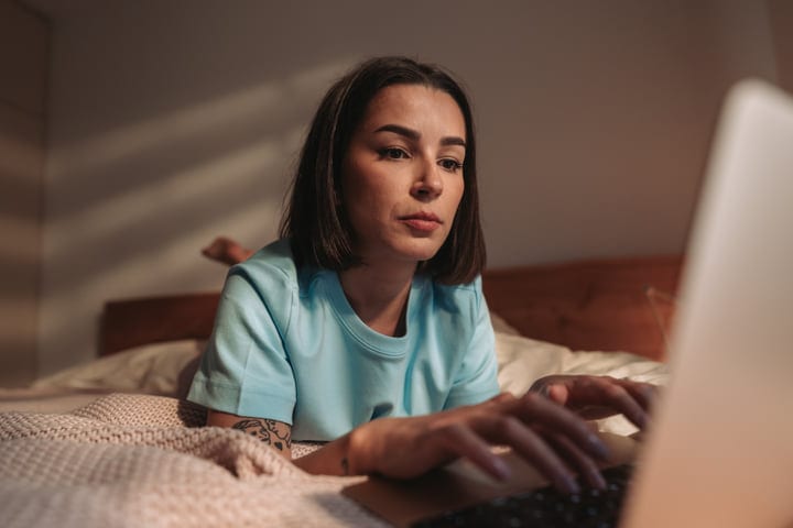 Focused Woman Works On Laptop From Bed During Her Morning Routine