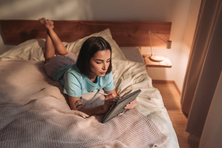Young Woman Lying In Bed Using Digital Tablet With Stylus