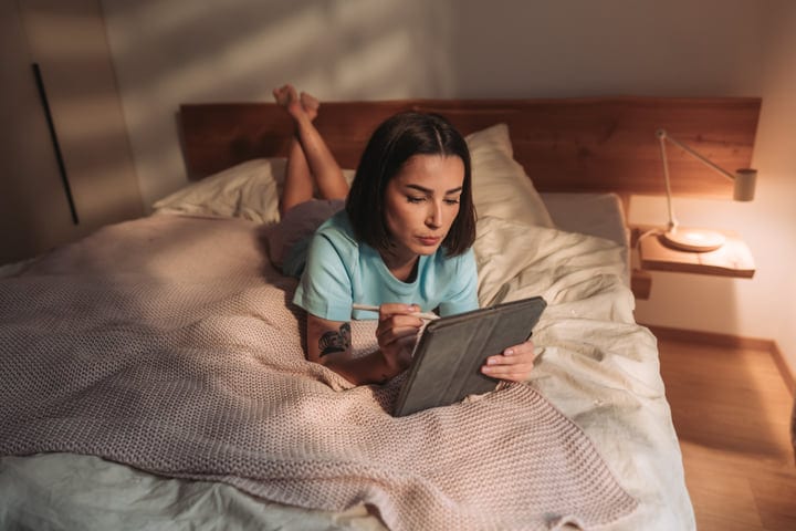 Woman Using Stylus On Tablet Lying In Bed In Morning Light