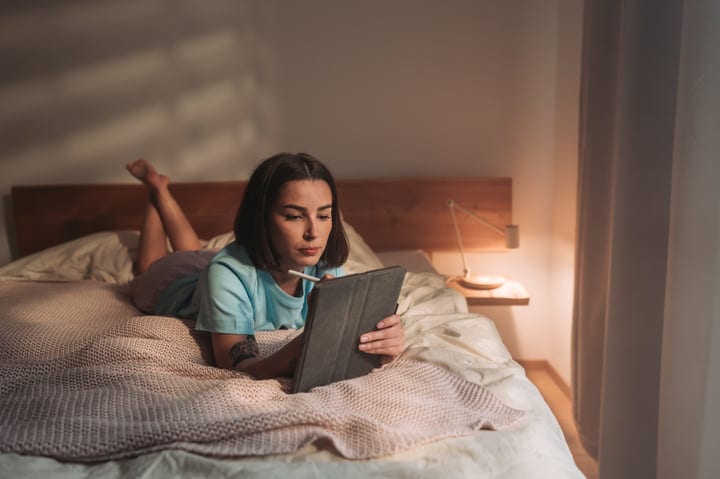 Young Woman Lying On Bed With Tablet In Cozy Morning Light