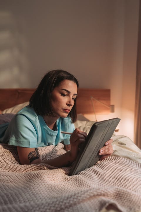 Woman In Light Blue T-Shirt Using Tablet And Stylus On Bed