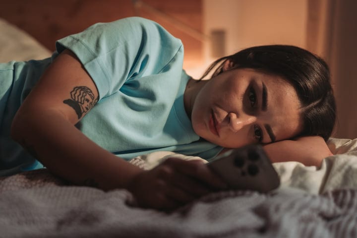 Young Woman Lying On Her Side In Bed With A Phone Near Her