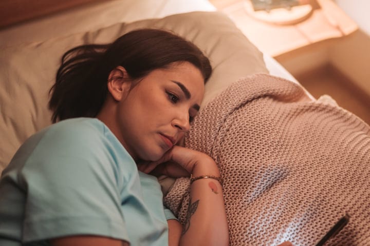 Young Woman Lies In Bed Under Warm Light During Her Morning Routine