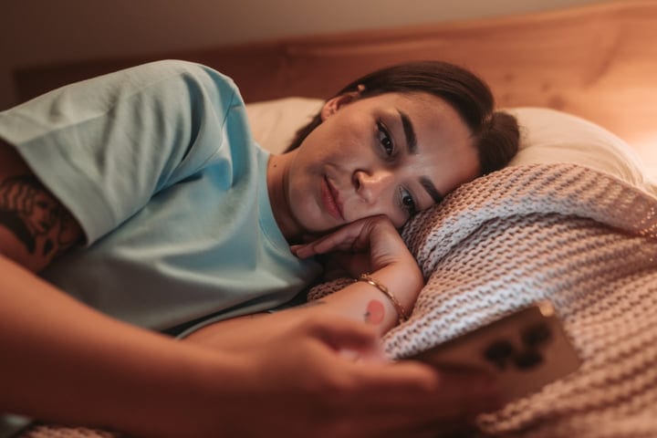Young Woman Lying In Bed With Smartphone In Soft Morning Light