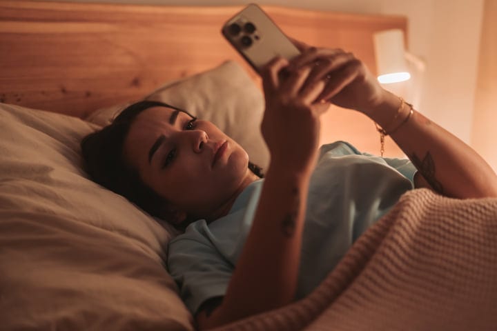 Young Woman Using Smartphone While Lying In Bed At Home