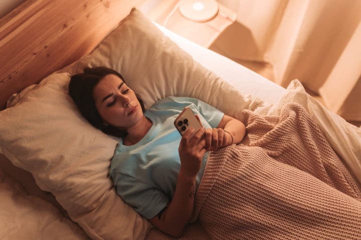 Young Woman Engaged With Her Phone Lying Comfortably In Bed