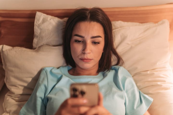 Relaxed Woman In Bed Scrolling Smartphone Screen In Soft Light
