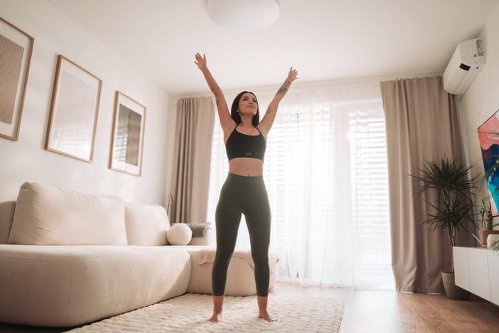 Woman In Green Sportswear Stretching Upwards In Bright Living Room