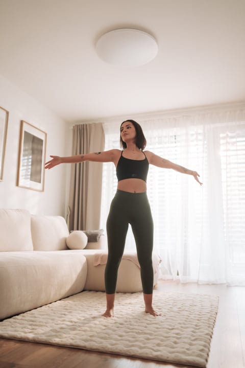 Young Woman Stretching Arms In Bright Modern Living Room During Morning Routine